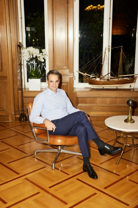 Kyriakos Mitsotakis sitting in a leather chair in an ornate office with wooden paneling and a model ship