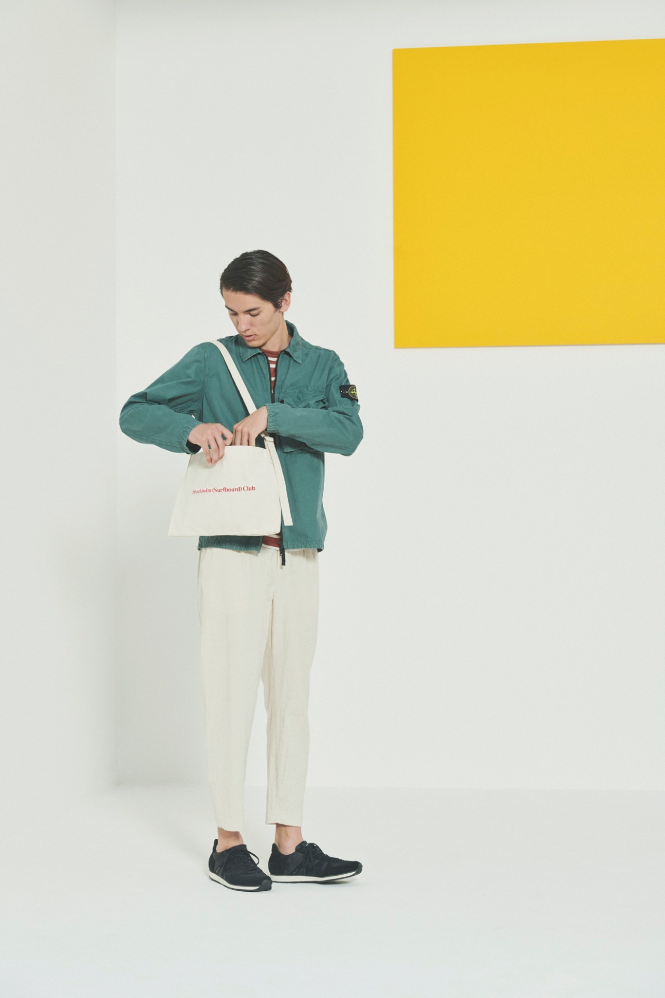 Model in smart-casual travel ensemble with teal jacket and cream trousers holding white tote bag