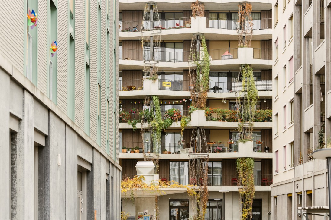 Multi-story residential building with green-planted balconies and climbing ivy at Mehr als Wohnen housing cooperative in Zurich.