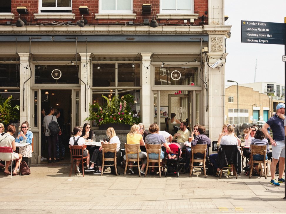 Outdoor seating area with diners at a London restaurant on a busy street.