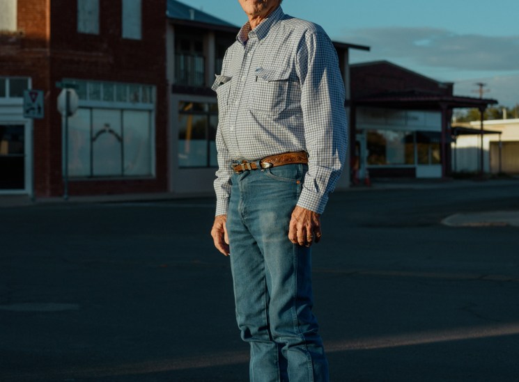 Man in cowboy hat and checkered shirt standing in front of brick buildings in Marfa, Texas.