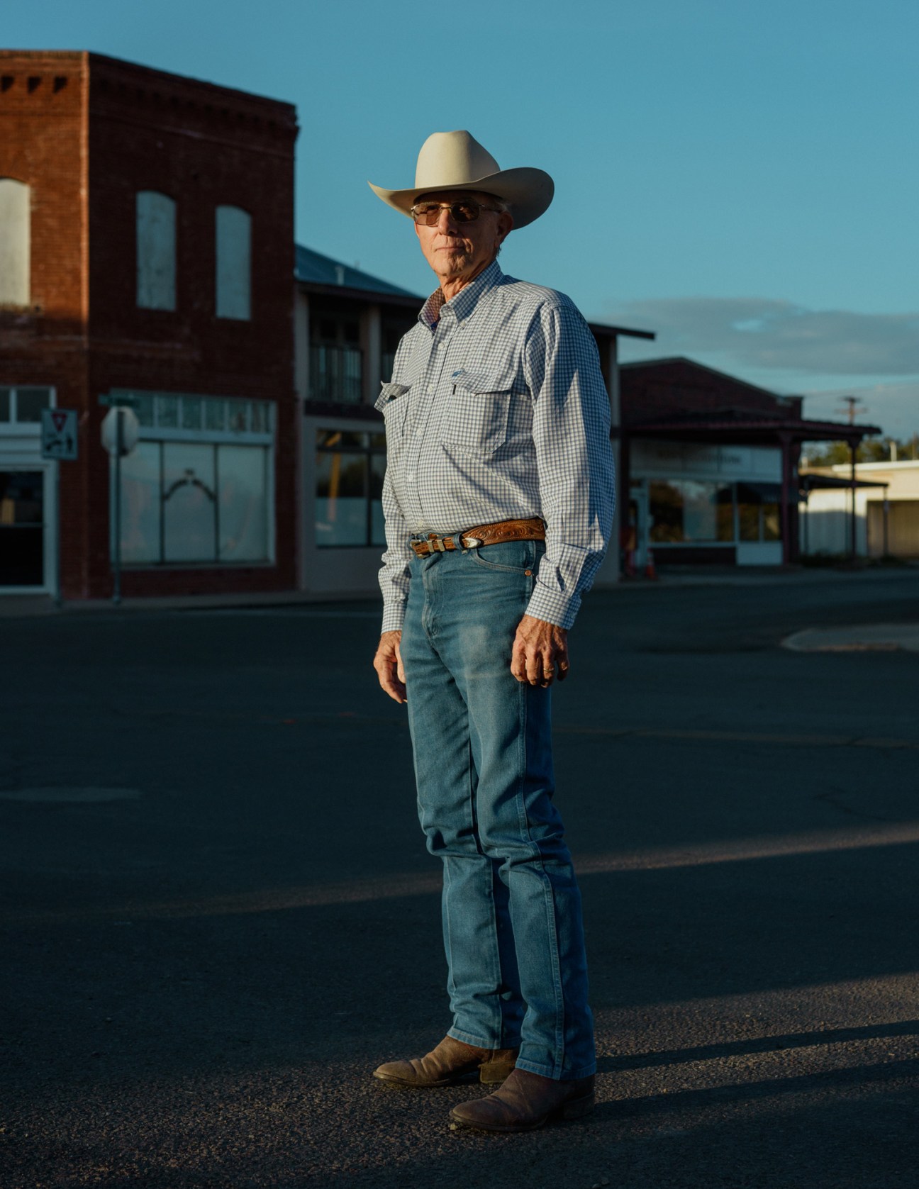 Man in cowboy hat and checkered shirt standing in front of brick buildings in Marfa, Texas.
