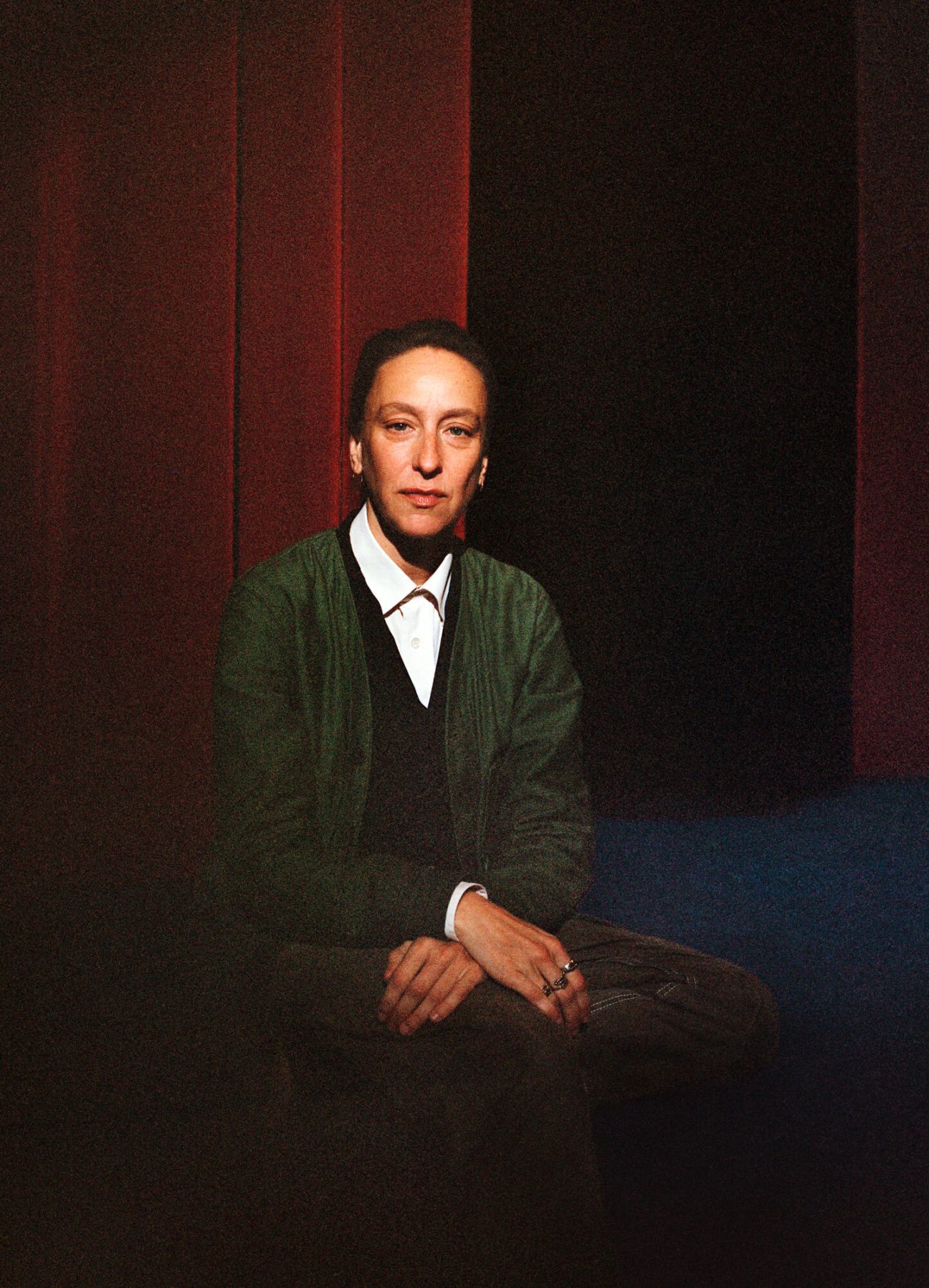 Portrait of French director Céline Sciamma wearing a green cardigan and white shirt, seated against a dark background