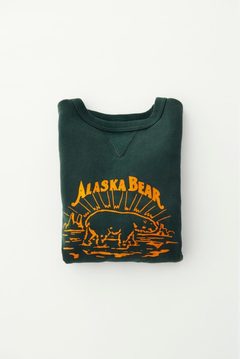 Dark green sweatshirt with yellow Alaska Bear graphic print laid flat on white background.
