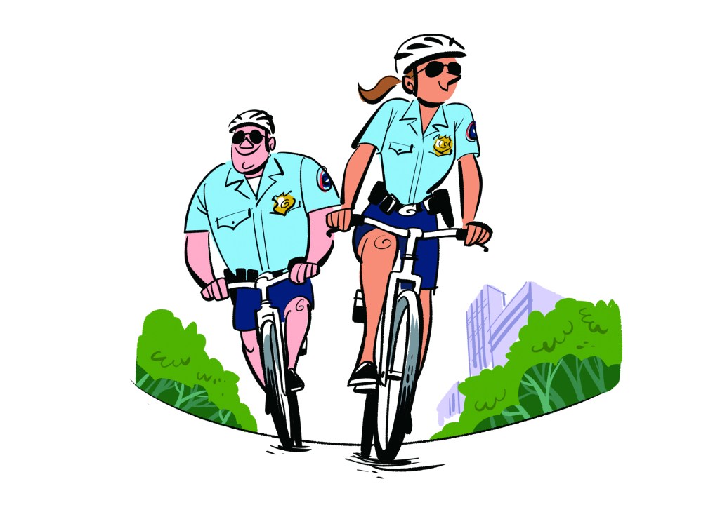 Two police officers on bicycles patrolling a city street wearing light blue uniforms and helmets