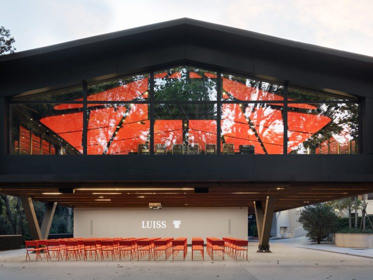 Modern two-storey Luiss university building with curved glass facade, dark exterior, elevated on pillars above open ground floor