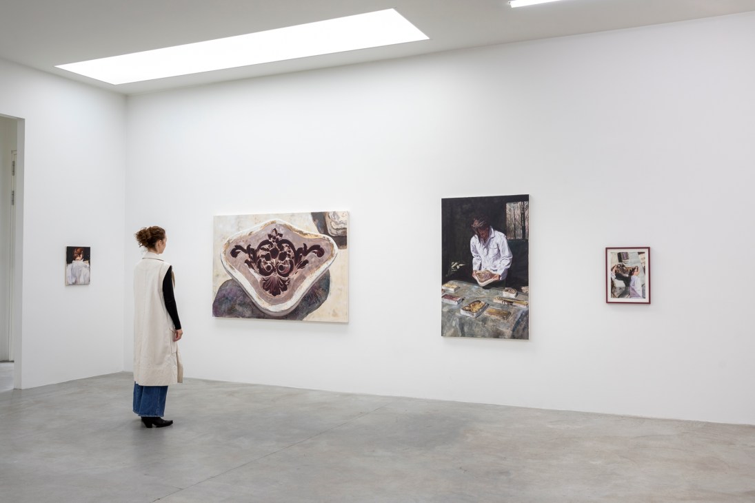 Person in white jacket and jeans viewing artworks on white gallery wall in minimalist exhibition space