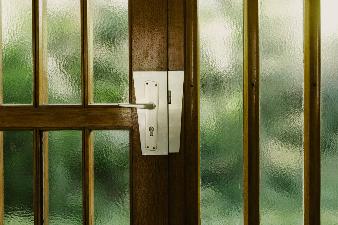 Mid-century door handle on wooden door with textured green glass panels.