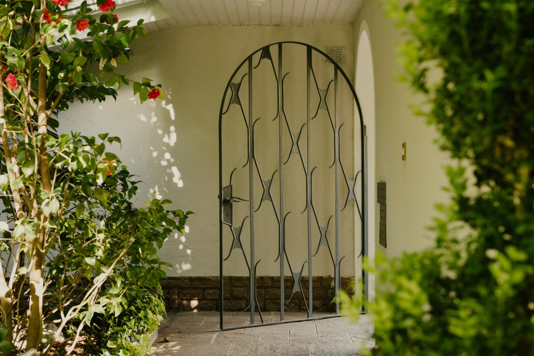 Ornate wrought-iron entrance gate with vine pattern in arched doorway surrounded by flowering plants.