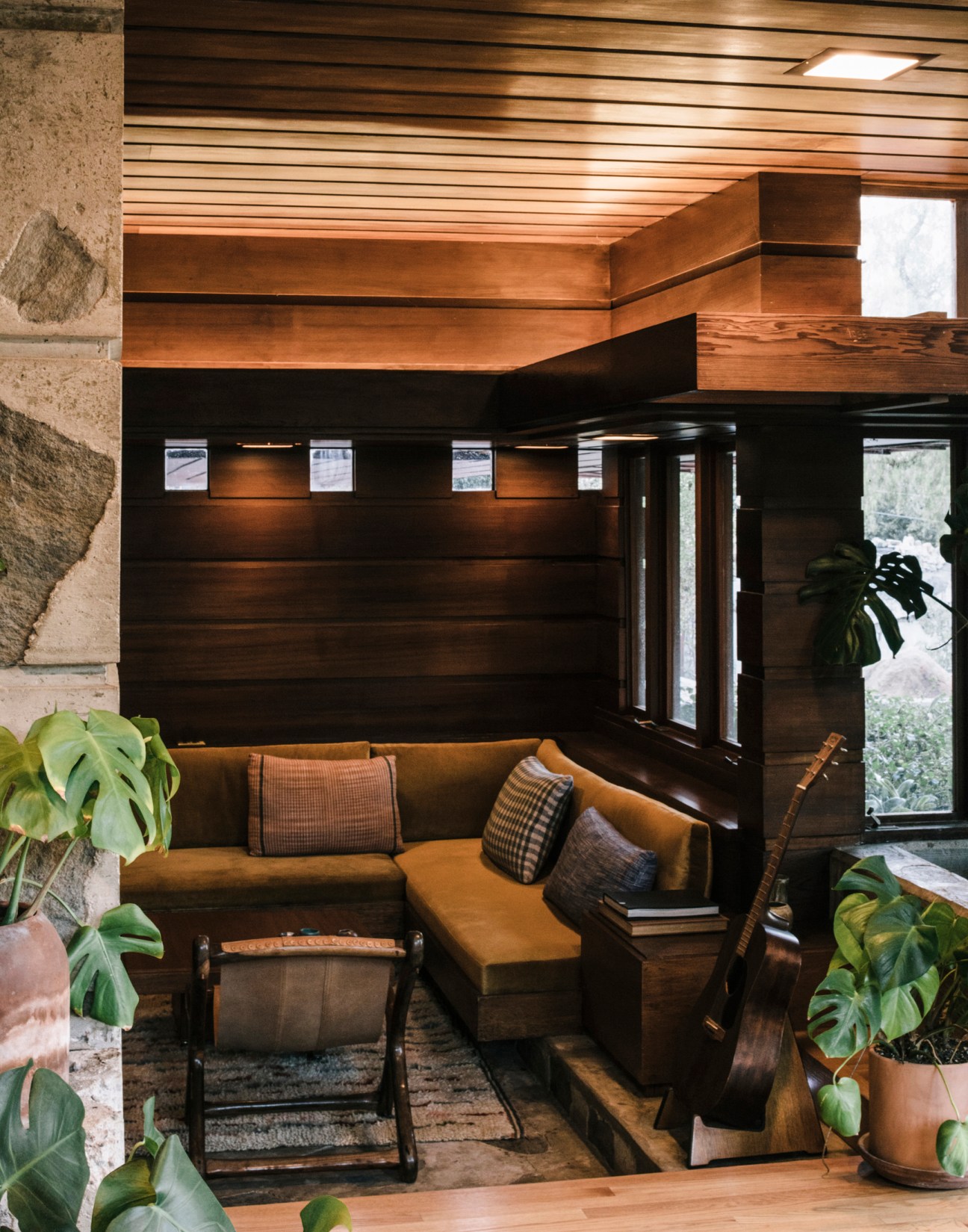 Anderson House living room designed by W Earl Wear, featuring a built-in sofa with ochre upholstery, dark wood paneling, and concrete fireplace.