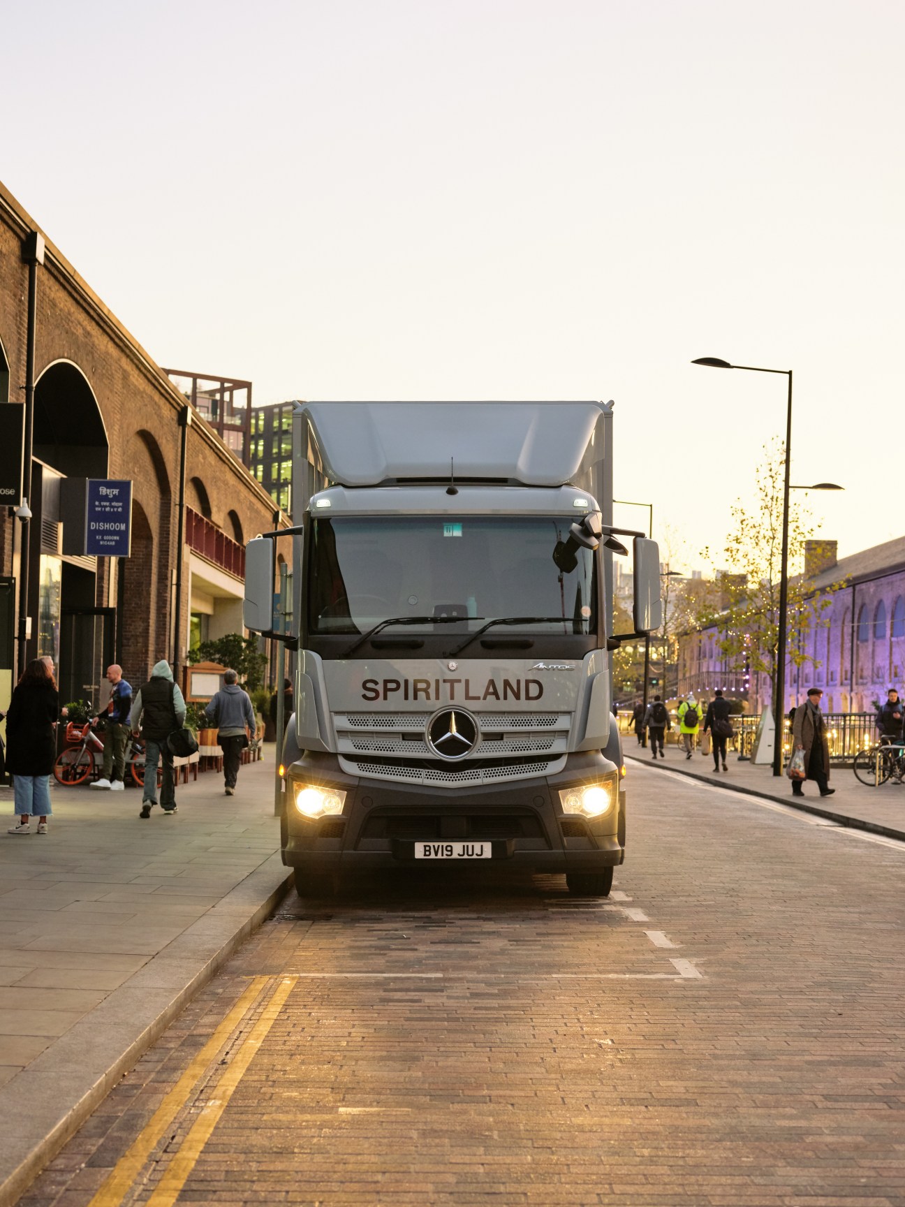 White Mercedes-Benz Spiritland truck parked on urban street with headlights on during golden hour