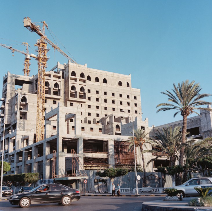 Construction site in Tripoli with concrete building structure, tower cranes, and palm trees
