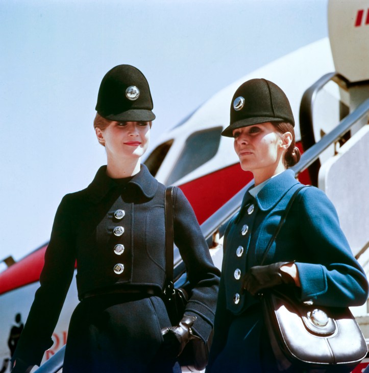 Two Iberia flight attendants in 1972 wearing Elio Berhanyer uniforms with large formal hats and double-breasted coats