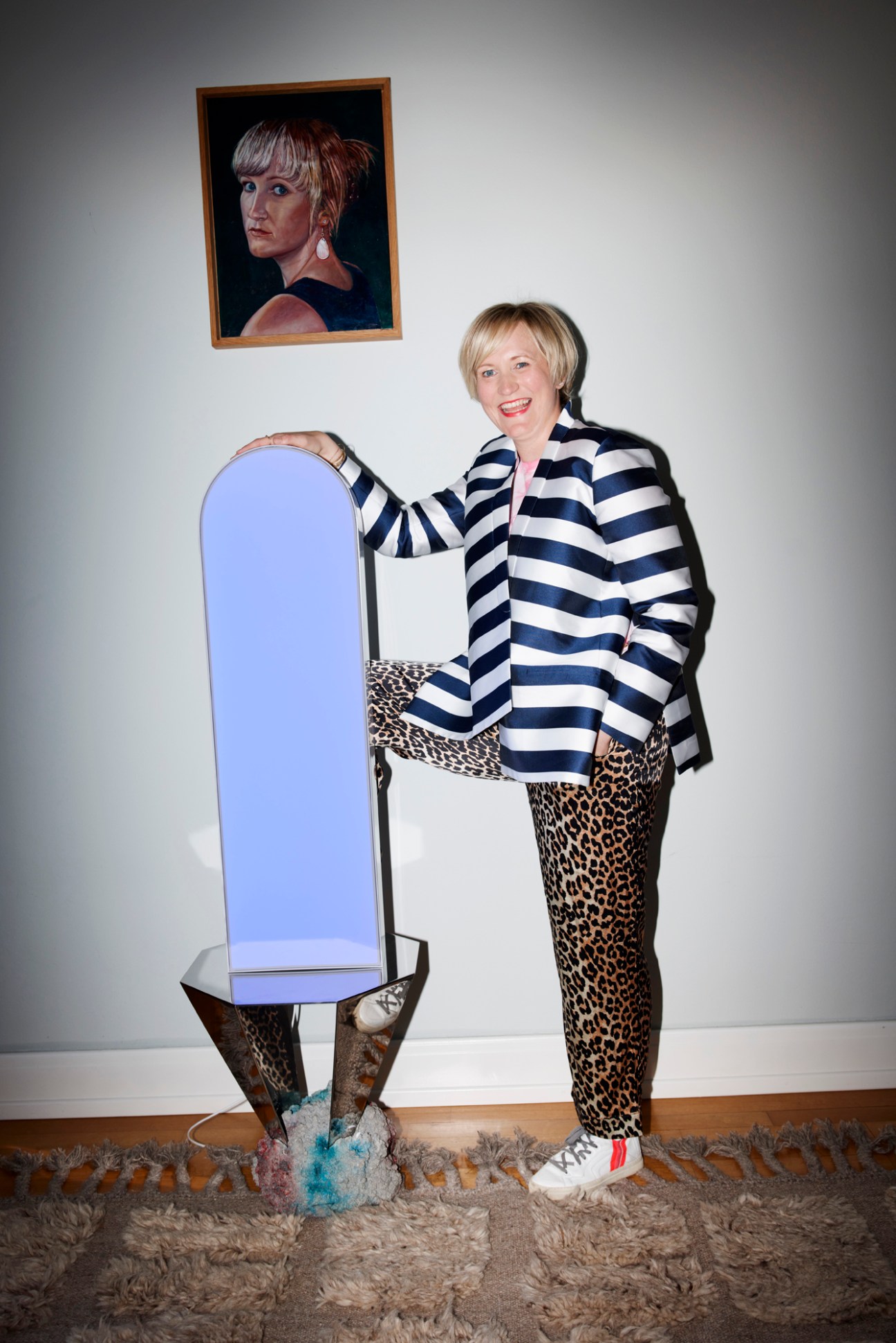 Woman in black and white striped blazer and leopard print pants standing next to full-length mirror in home