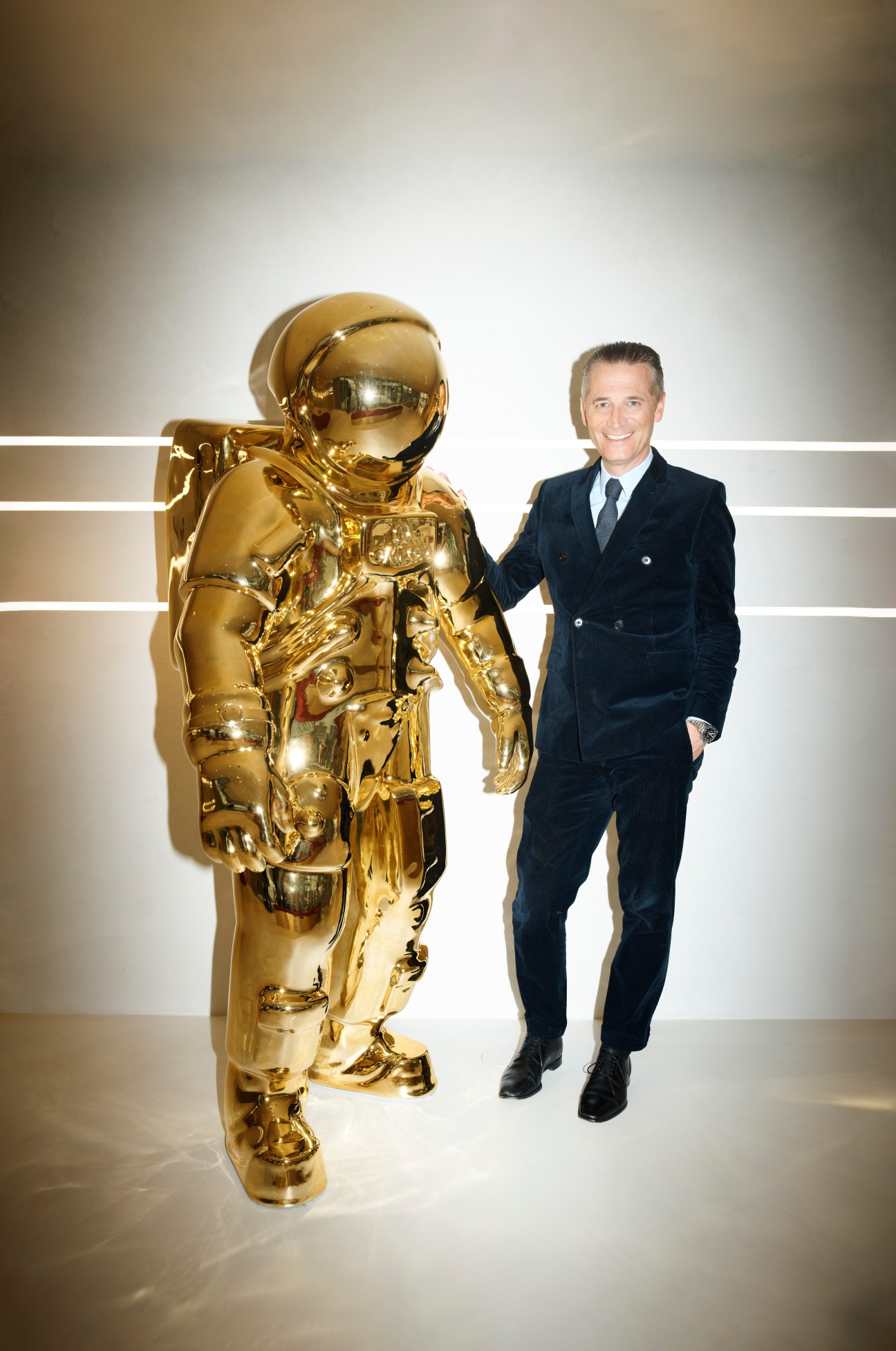 Raynald Aeschlimann in a dark suit standing next to a golden astronaut sculpture in a modern retail space