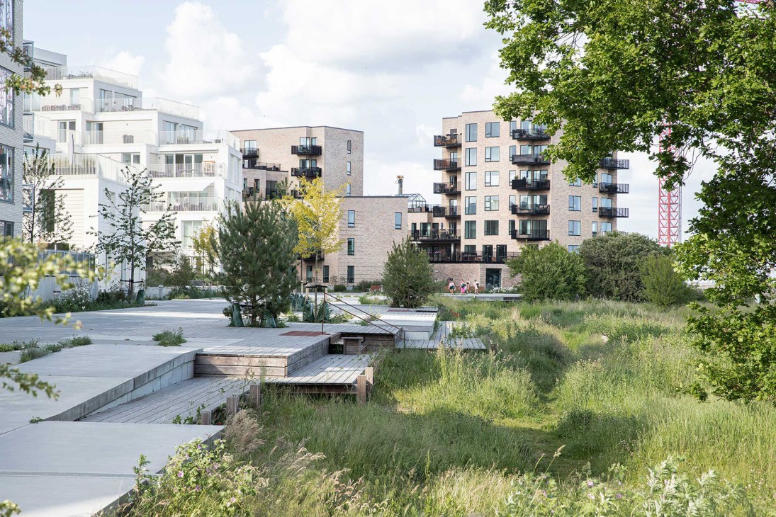 Modern residential buildings with balconies overlooking landscaped green spaces and wooden walkways