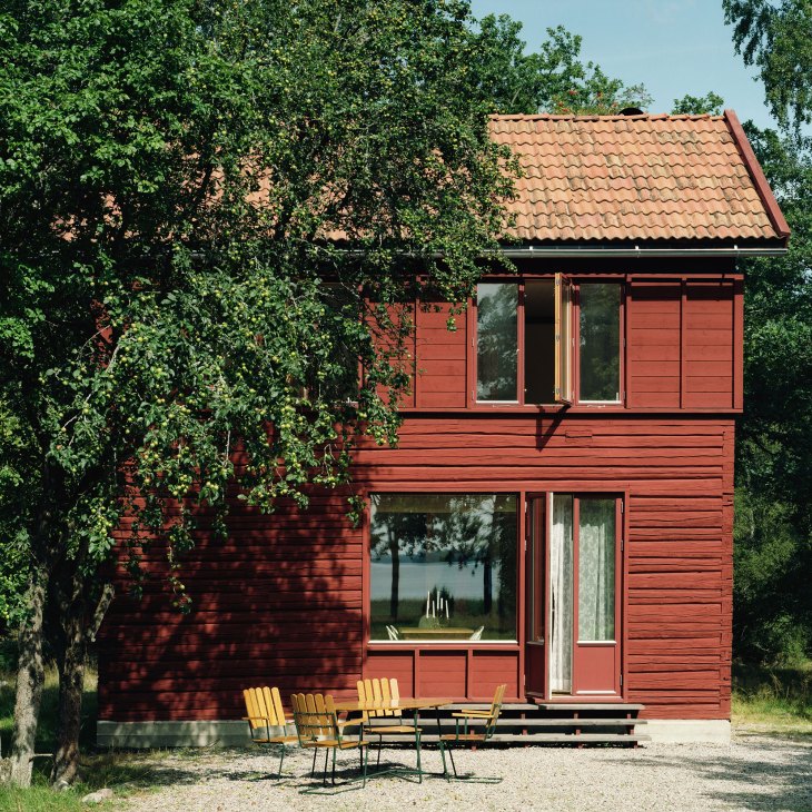 Red wooden house surrounded by green foliage with yellow chairs on the porch.