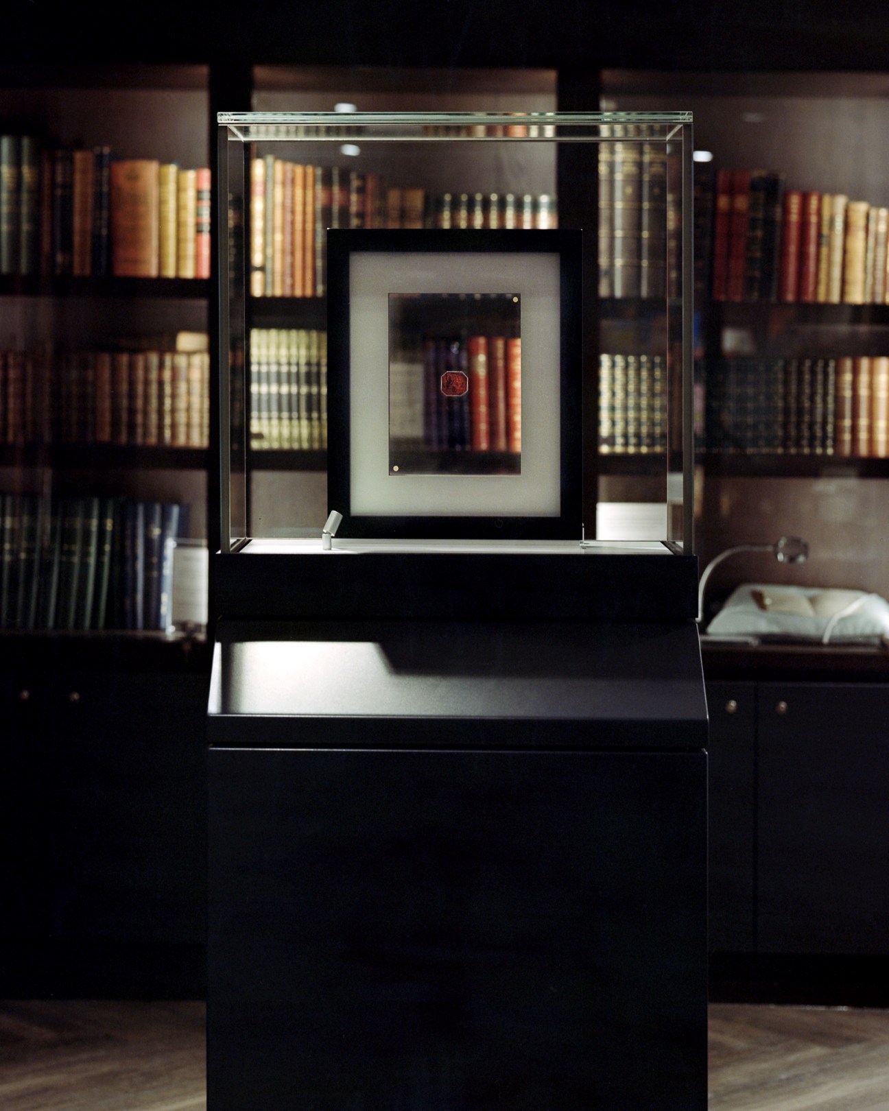 Glass display case containing a rare stamp in a library setting with bookshelves in the background