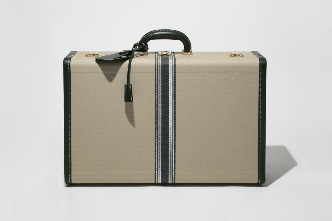 Beige canvas suitcase with dark green leather trim and brass hardware, featuring striped detailing