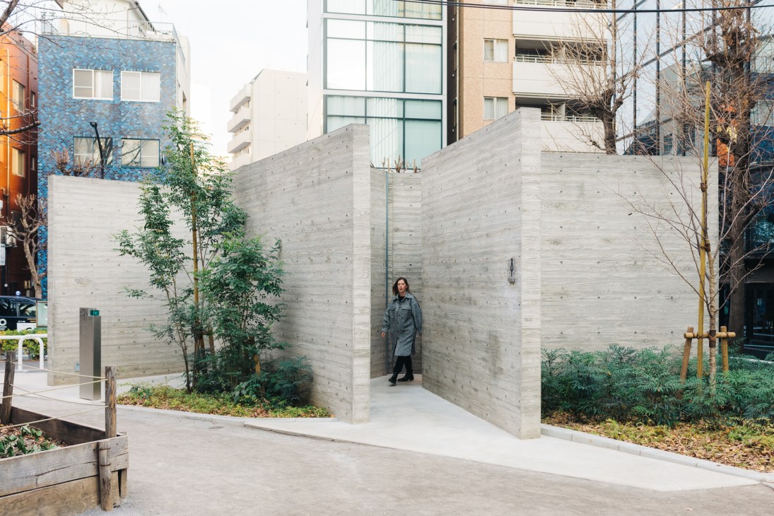 Person standing in doorway of concrete public toilet building with geometric angular walls