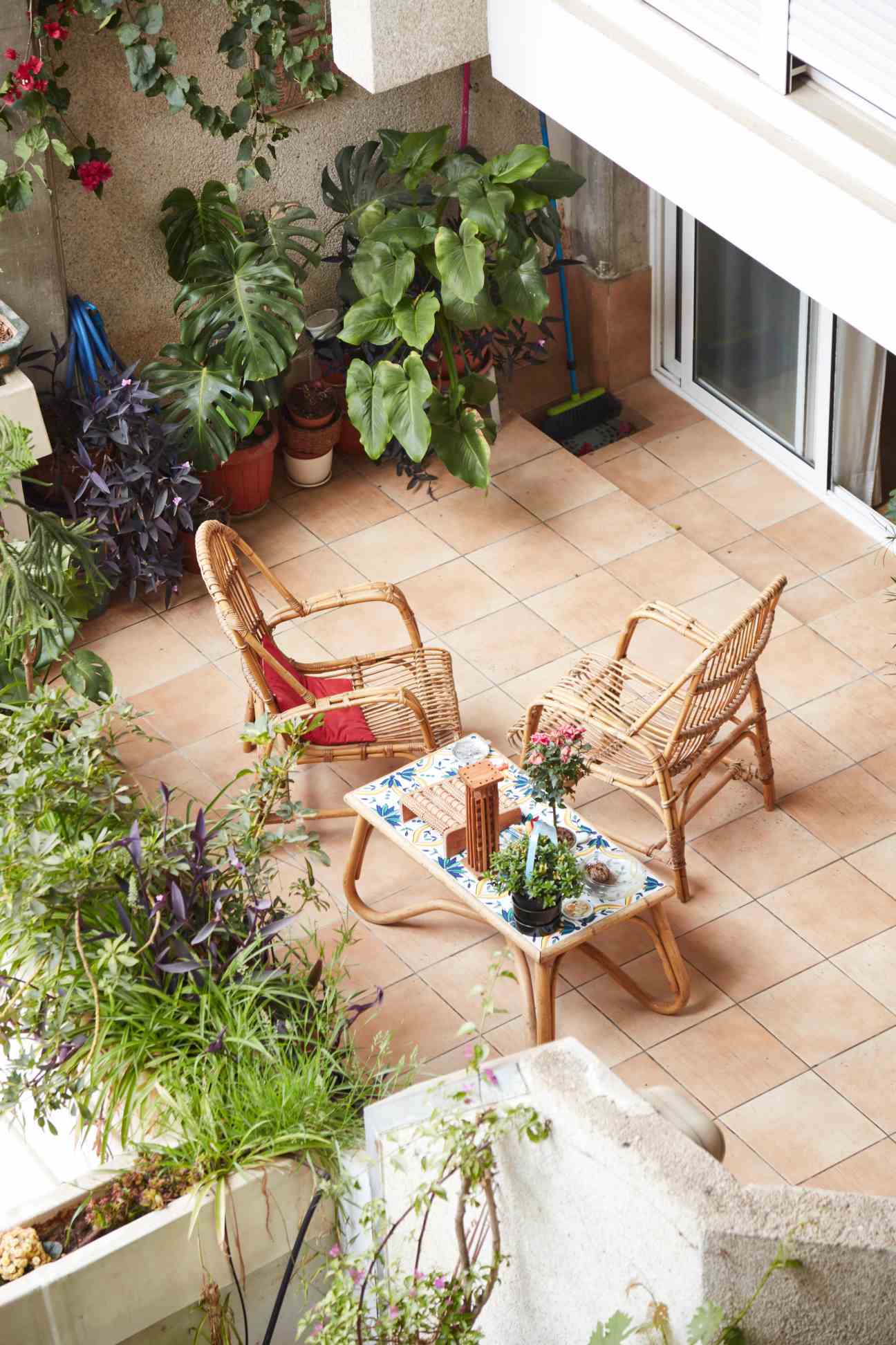 Overhead view of a roof terrace with potted plants, two wicker chairs with red cushions, and a small decorative table.