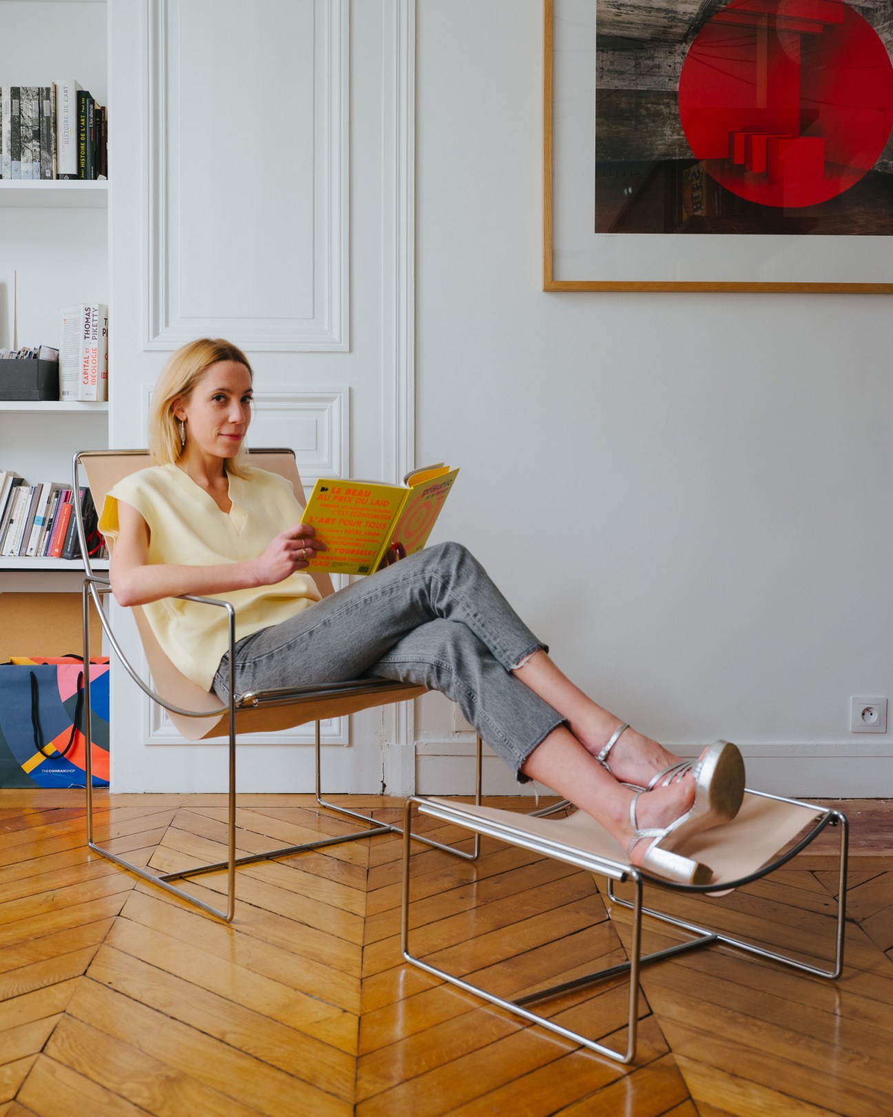 Léonie Alma Mason sitting in modern chair reading yellow book in bright interior with parquet floors