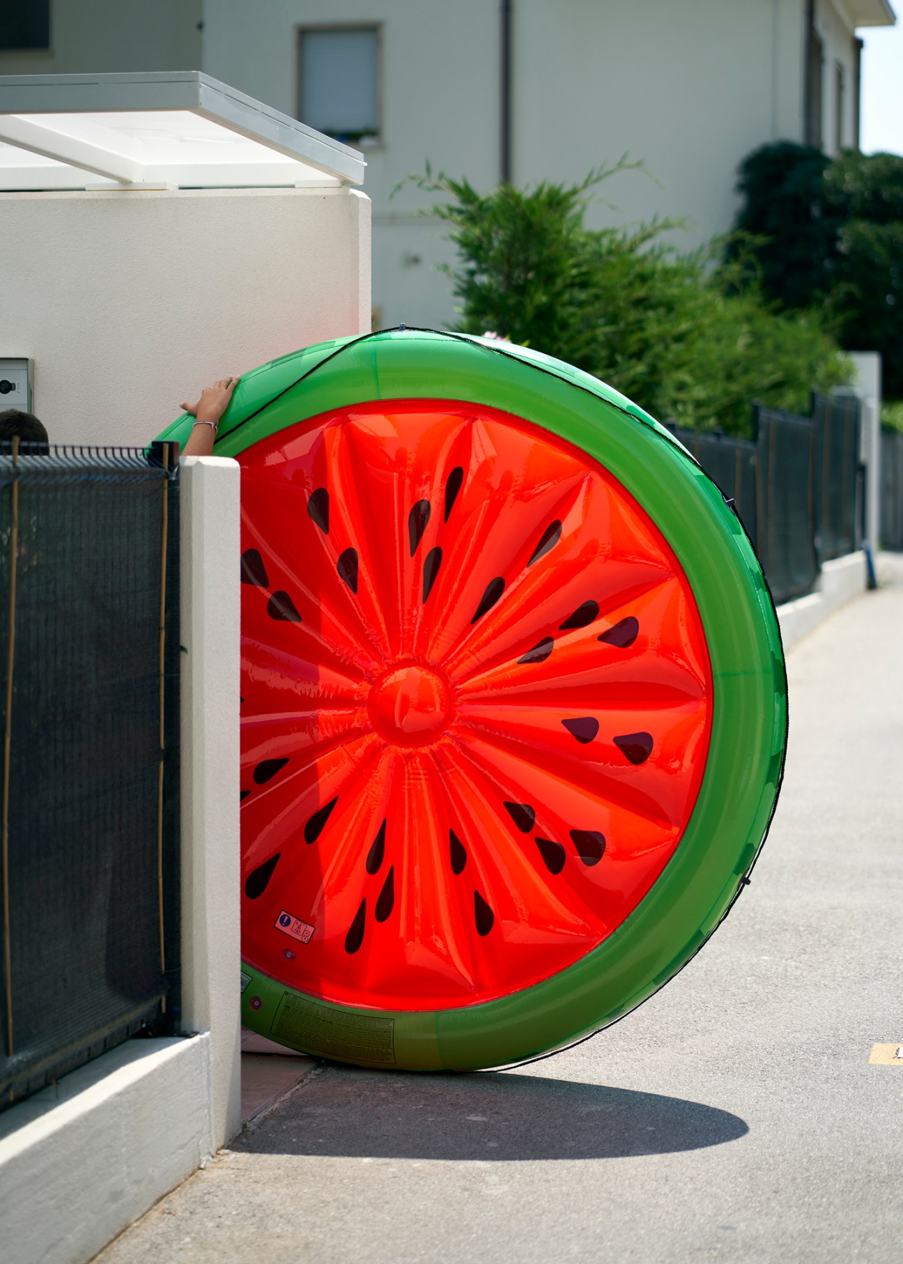 Large inflatable watermelon slice float leaning against a fence on a concrete surface