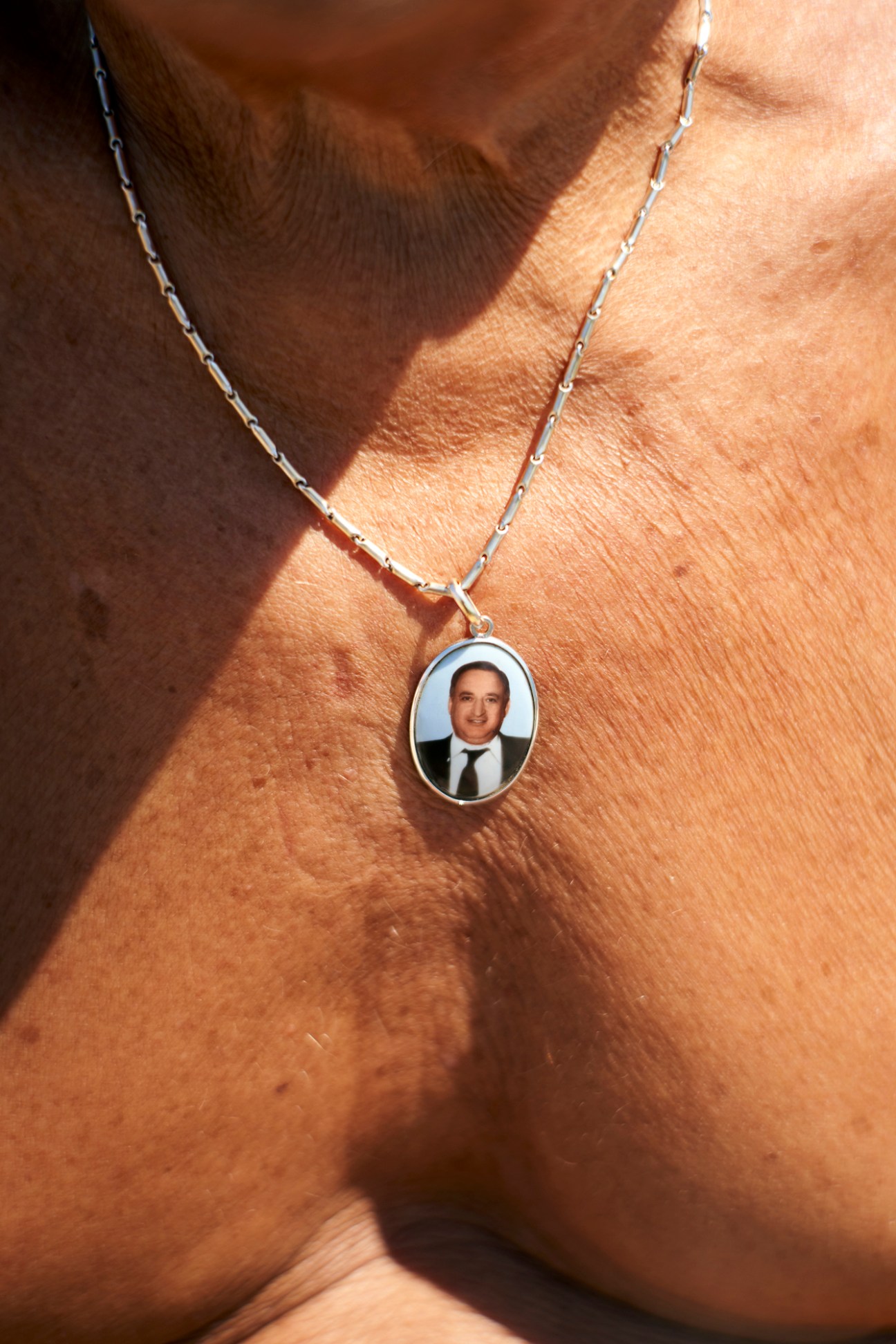 Silver chain necklace with oval pendant containing portrait photo of smiling man in suit worn on tanned skin
