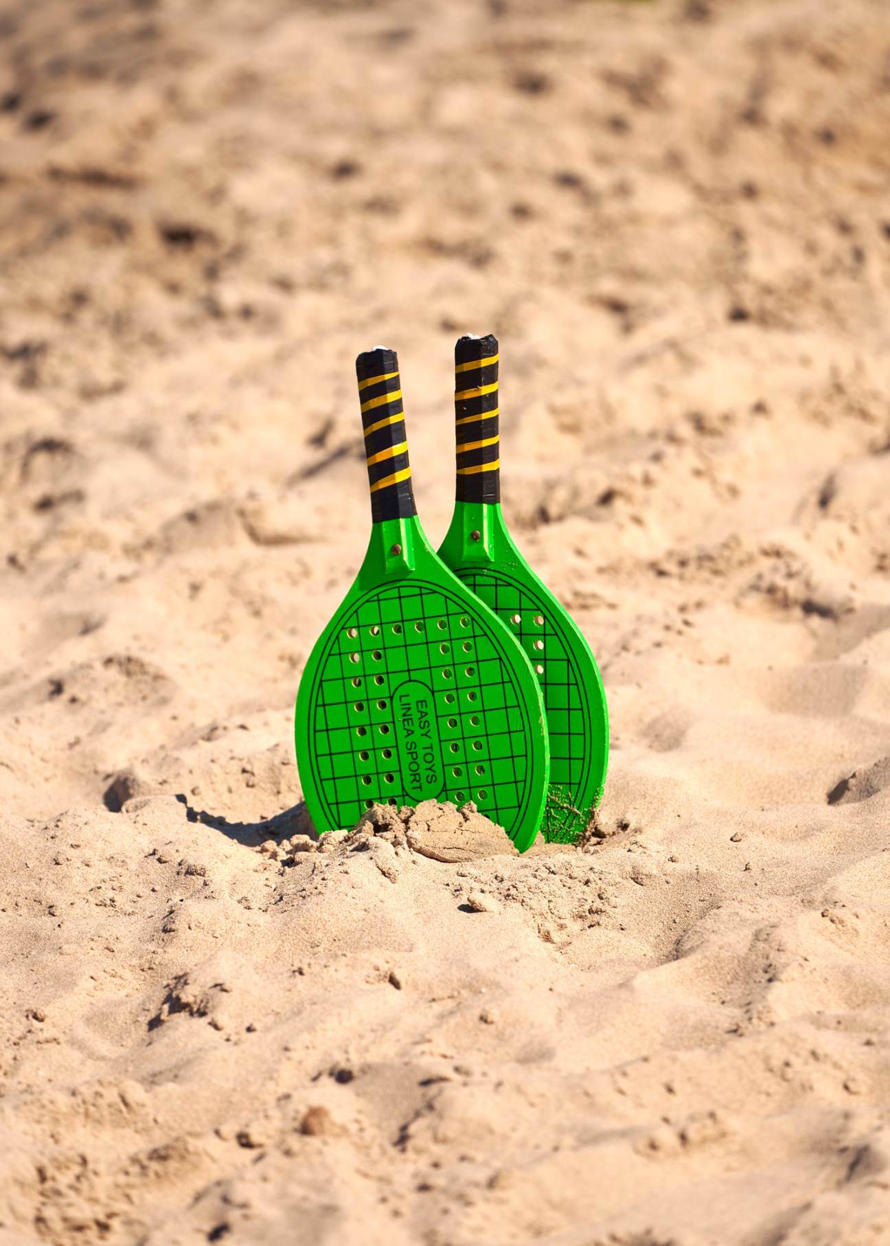 Two green beach tennis rackets stuck in sand with black and yellow striped handles