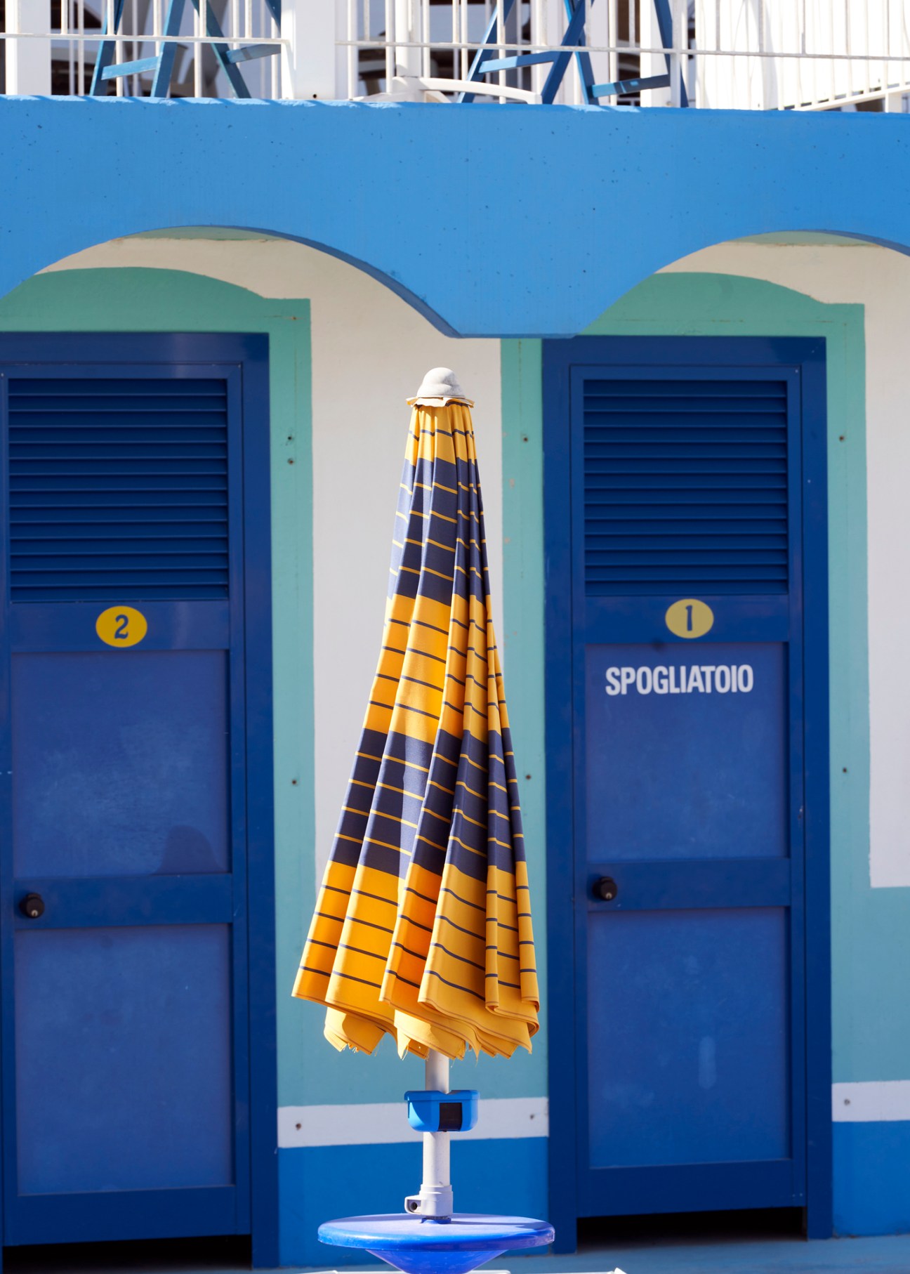 Blue and white beach changing rooms with closed striped umbrella at Italian beach establishment