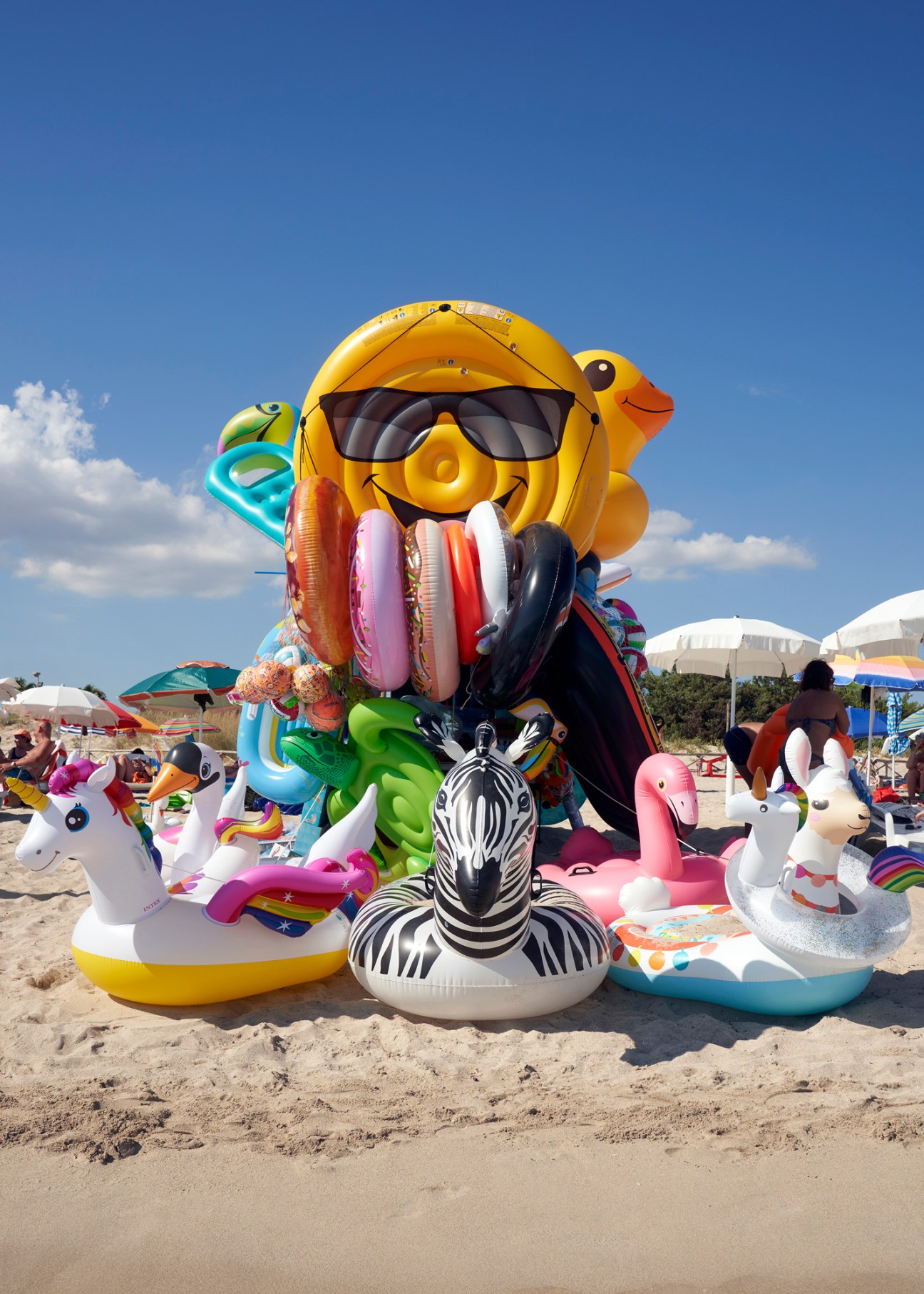 Colorful inflatable pool floats and toys including sunglasses emoji, zebra, flamingo arranged on sandy beach