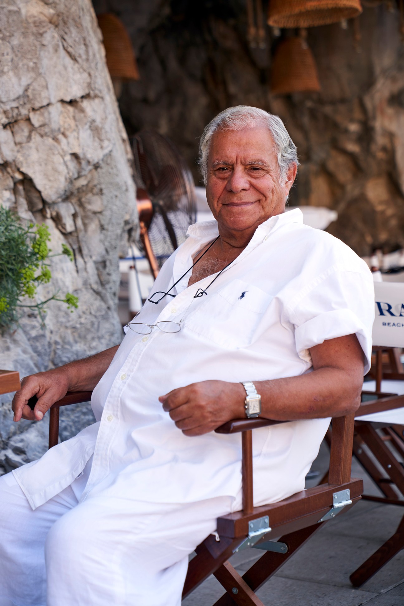 Salvatore, an older man in white clothing, sitting relaxed in a wooden chair at a coastal location in Positano