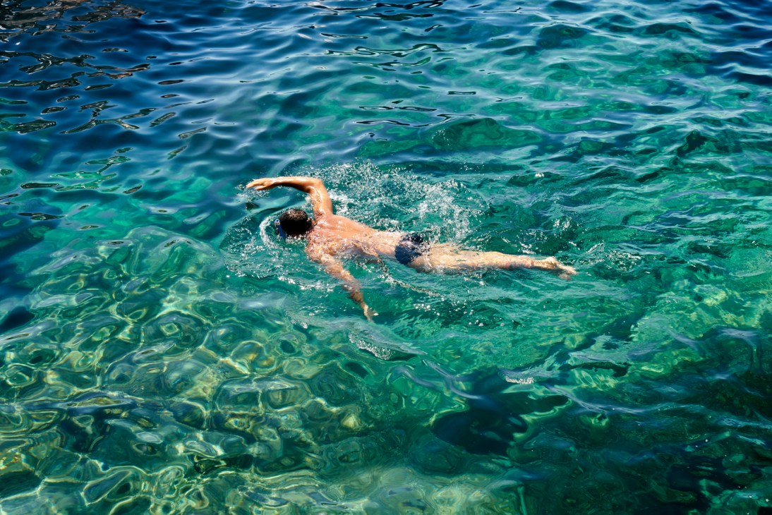 Swimmer doing front crawl stroke in crystal clear turquoise Mediterranean waters