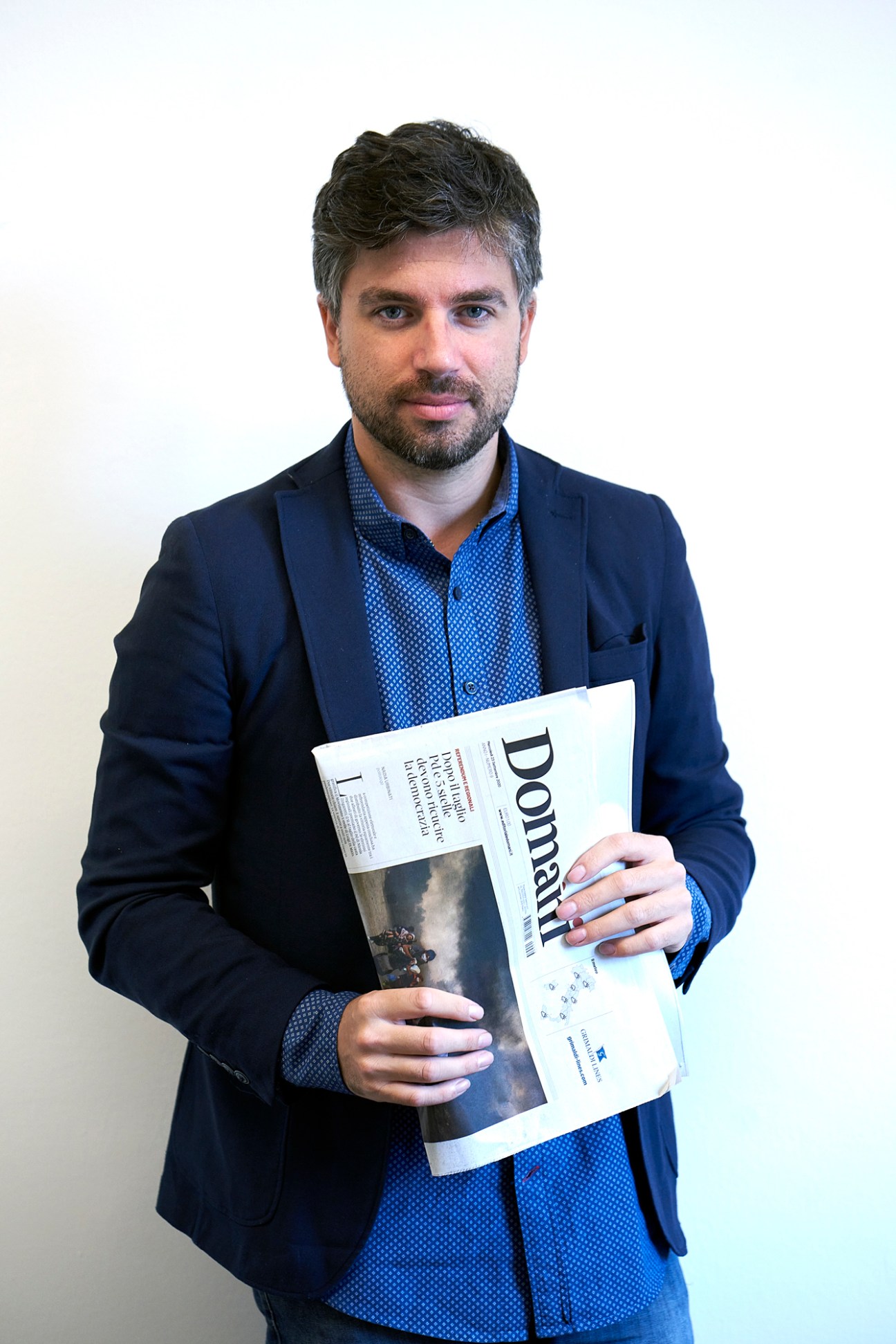 Stefano Feltri, editor of Domani newspaper, holds a copy of the publication while standing against a white background.