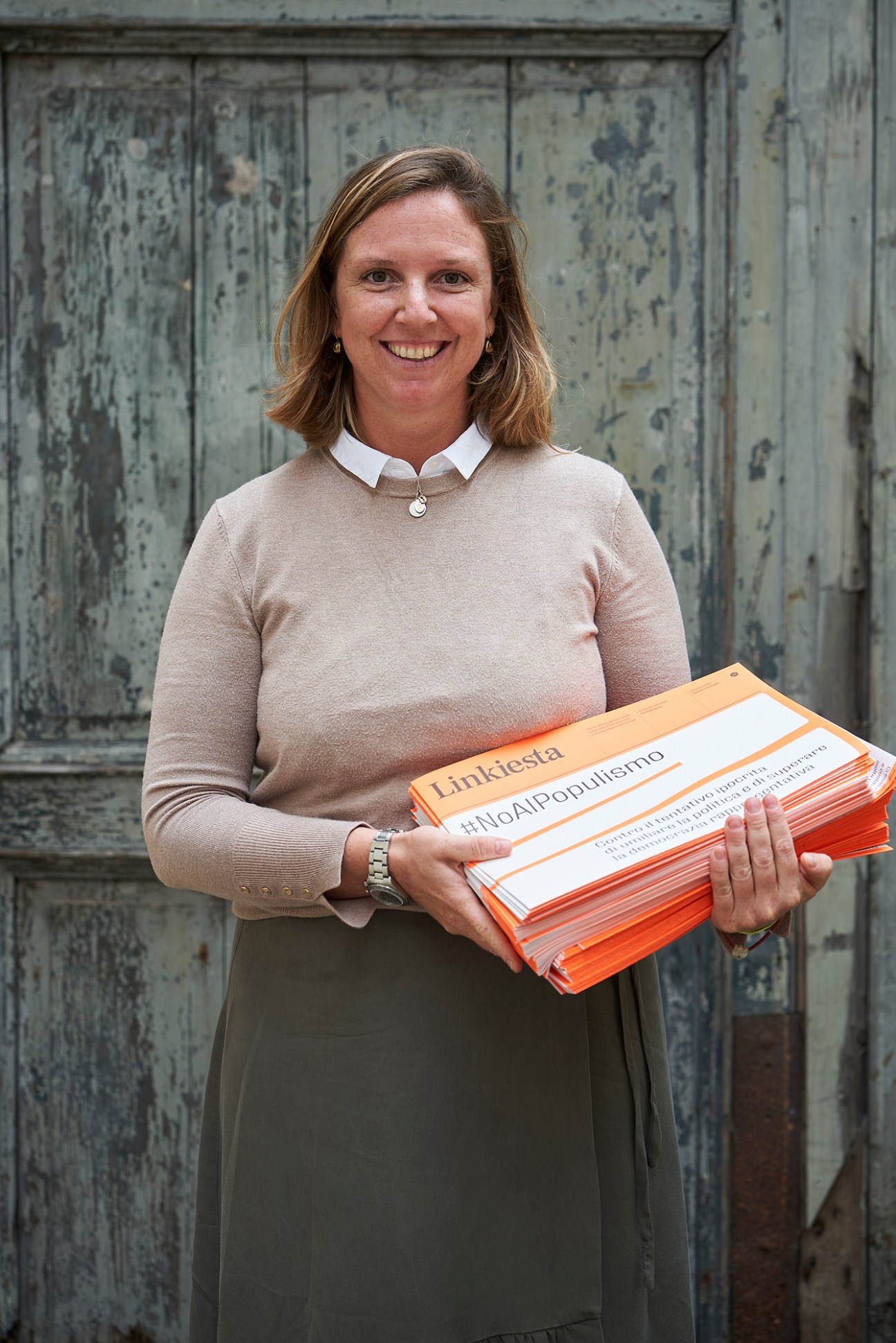 Woman holding stacks of orange and white Linkiesta newspapers with #NoAlPopulismo hashtag visible.