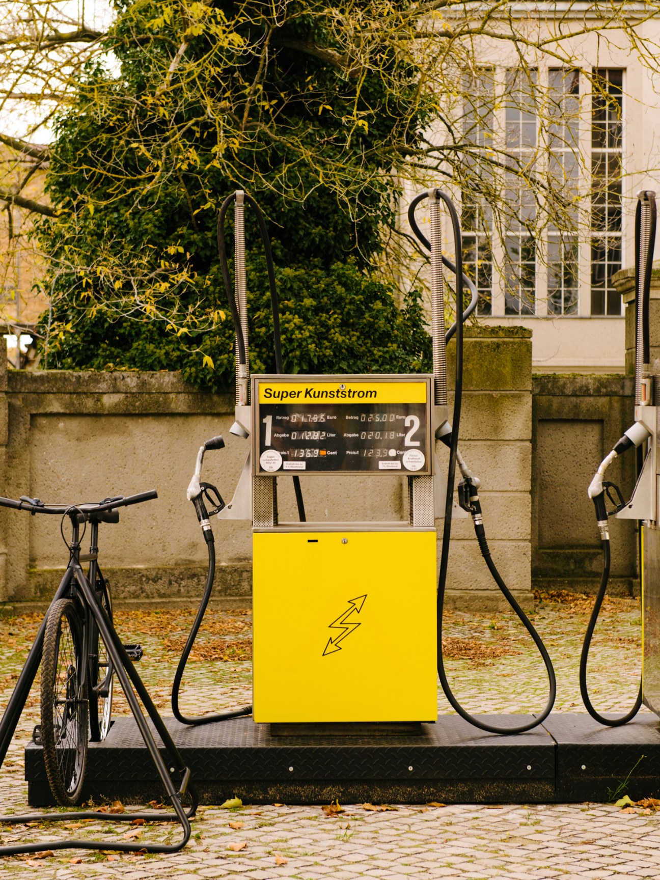 Yellow electric bike charging station with Super Kunststrom branding and lightning bolt symbol on a cobblestone street