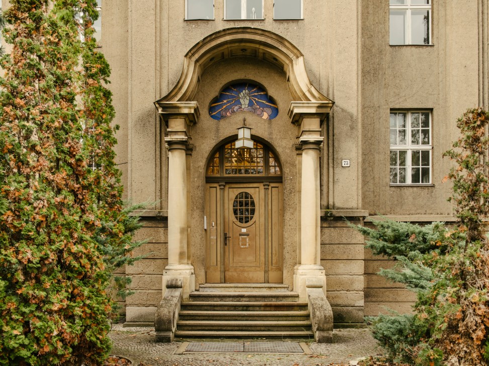 Entrance to historic brick building with ornate arched doorway, columns, and decorative stained glass window above