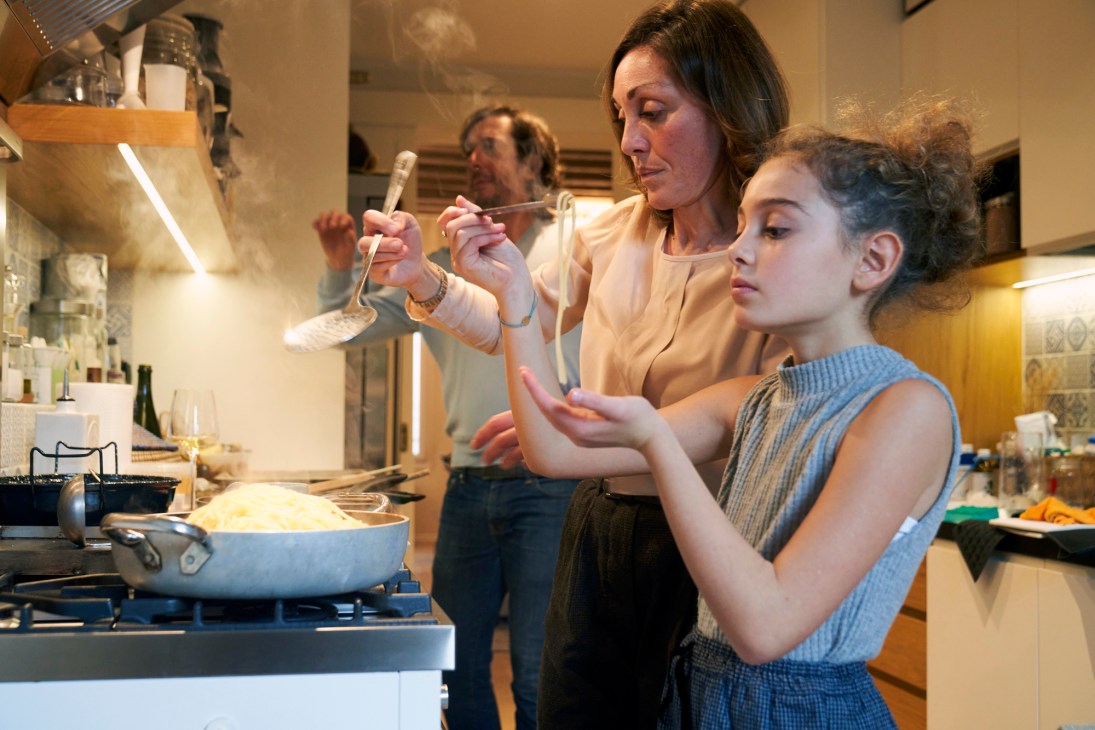 Woman and young girl cooking together in a kitchen, tasting food from a spoon