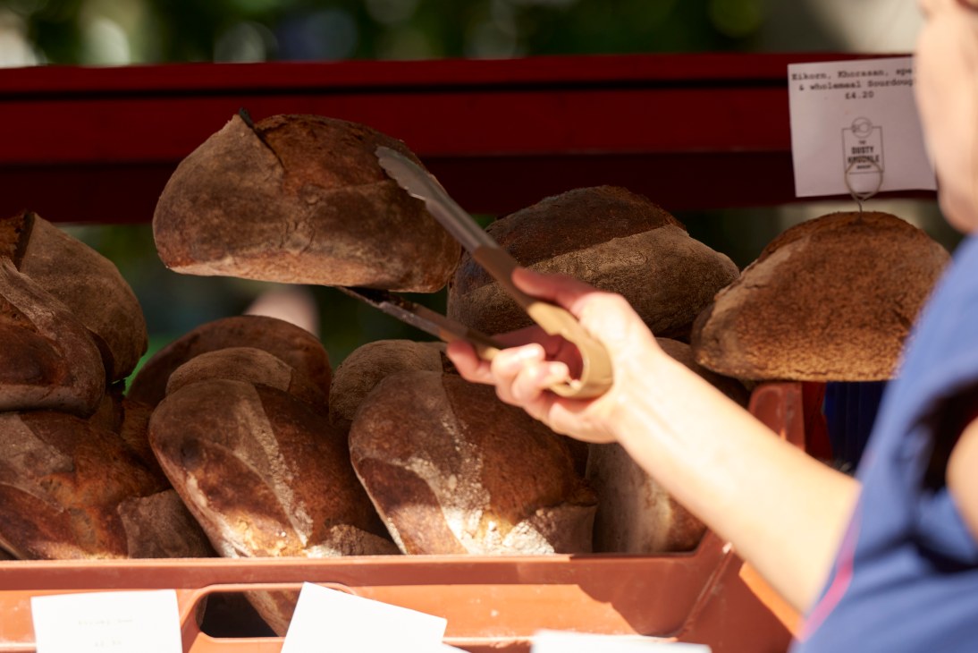 Hand selecting dark rye bread from wooden display case at bakery