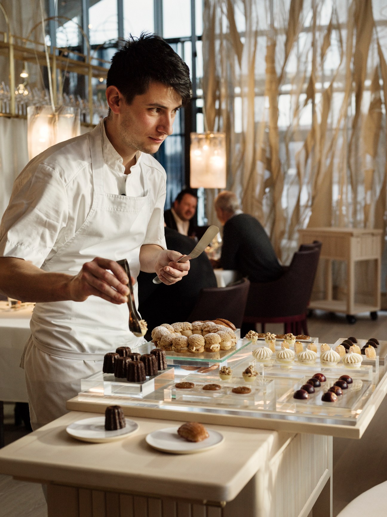 Chef in white uniform carefully plating petit fours and chocolates on glass display trays