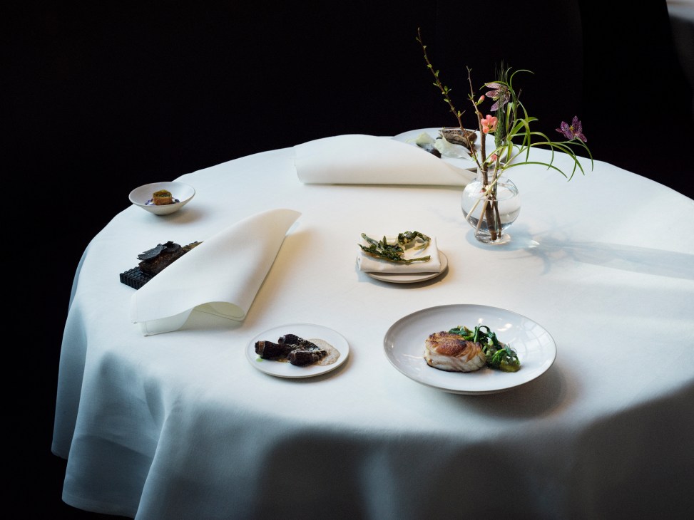 White tablecloth with plated dishes, small bowls, decorative arrangements and folded napkin on dining table