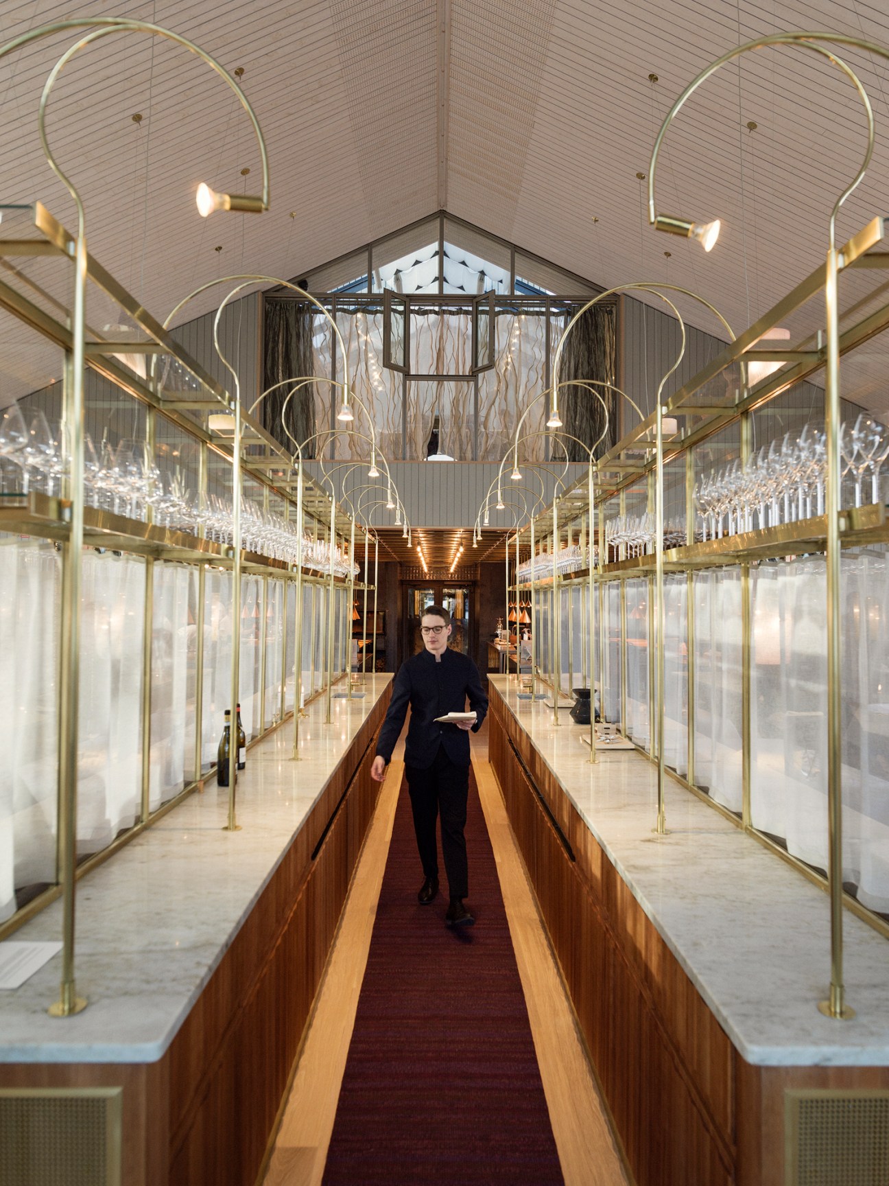 Restaurant dining room with brass curved light fixtures and glass partitions, showing private dining space on upper level