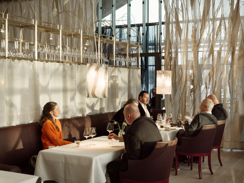 Diners seated at white-clothed tables in modern restaurant with decorative ceiling elements and warm lighting