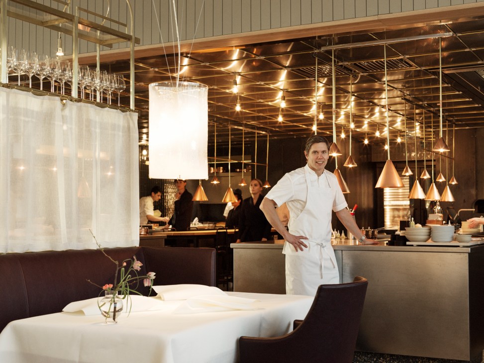 Chef Tommy Myllymäki in white chef's coat standing confidently in his restaurant's dining room
