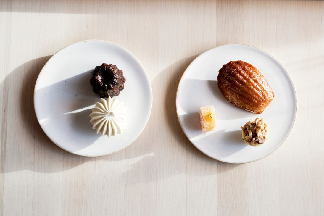 Two white plates with elegant small pastries and desserts arranged artfully on a light wooden surface