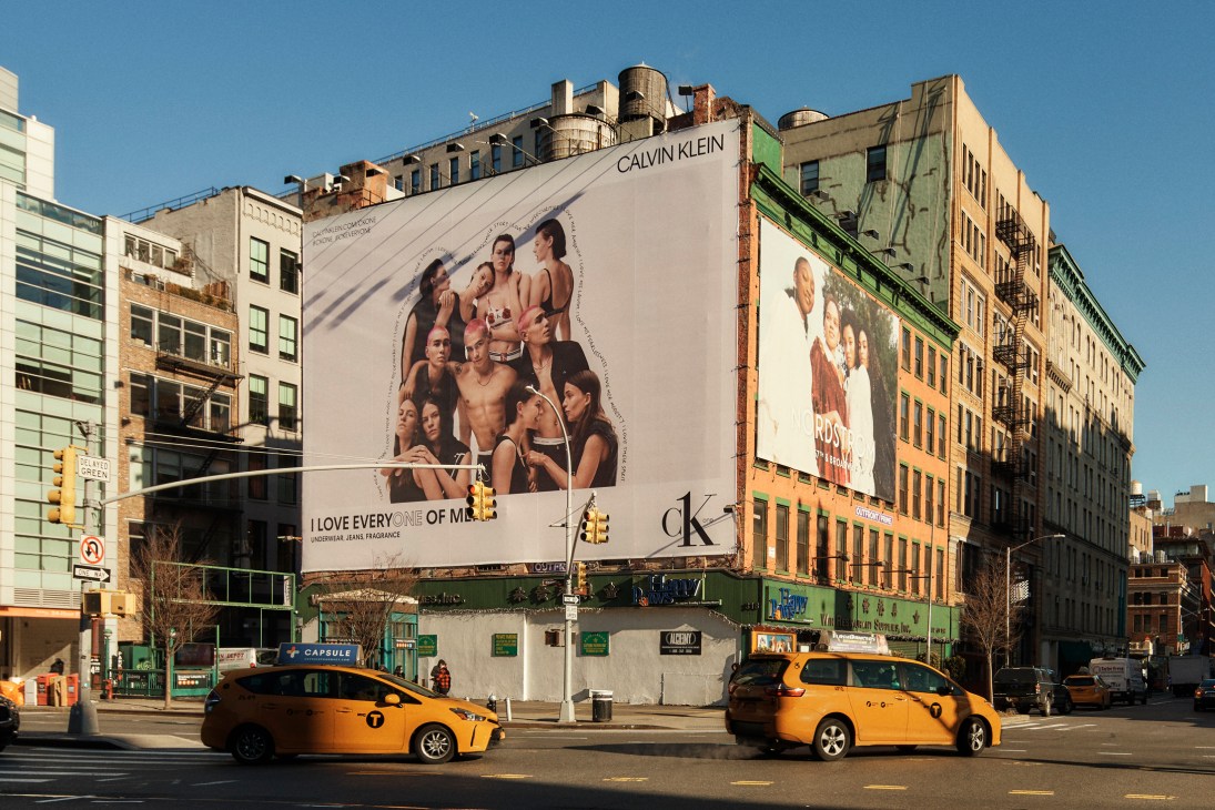 Large Calvin Klein billboard advertisement on a building corner in downtown Manhattan with yellow taxis passing below