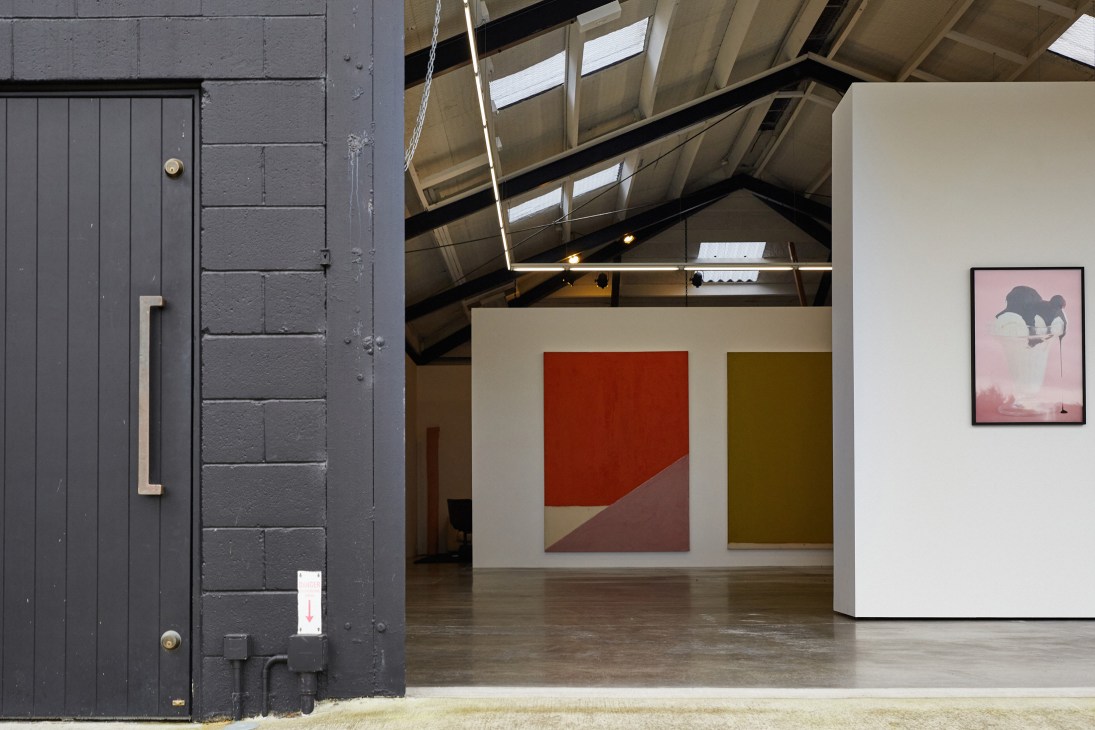 Interior of Tim Melville Gallery with industrial ceiling, artworks displayed on white walls, and dark entrance door.