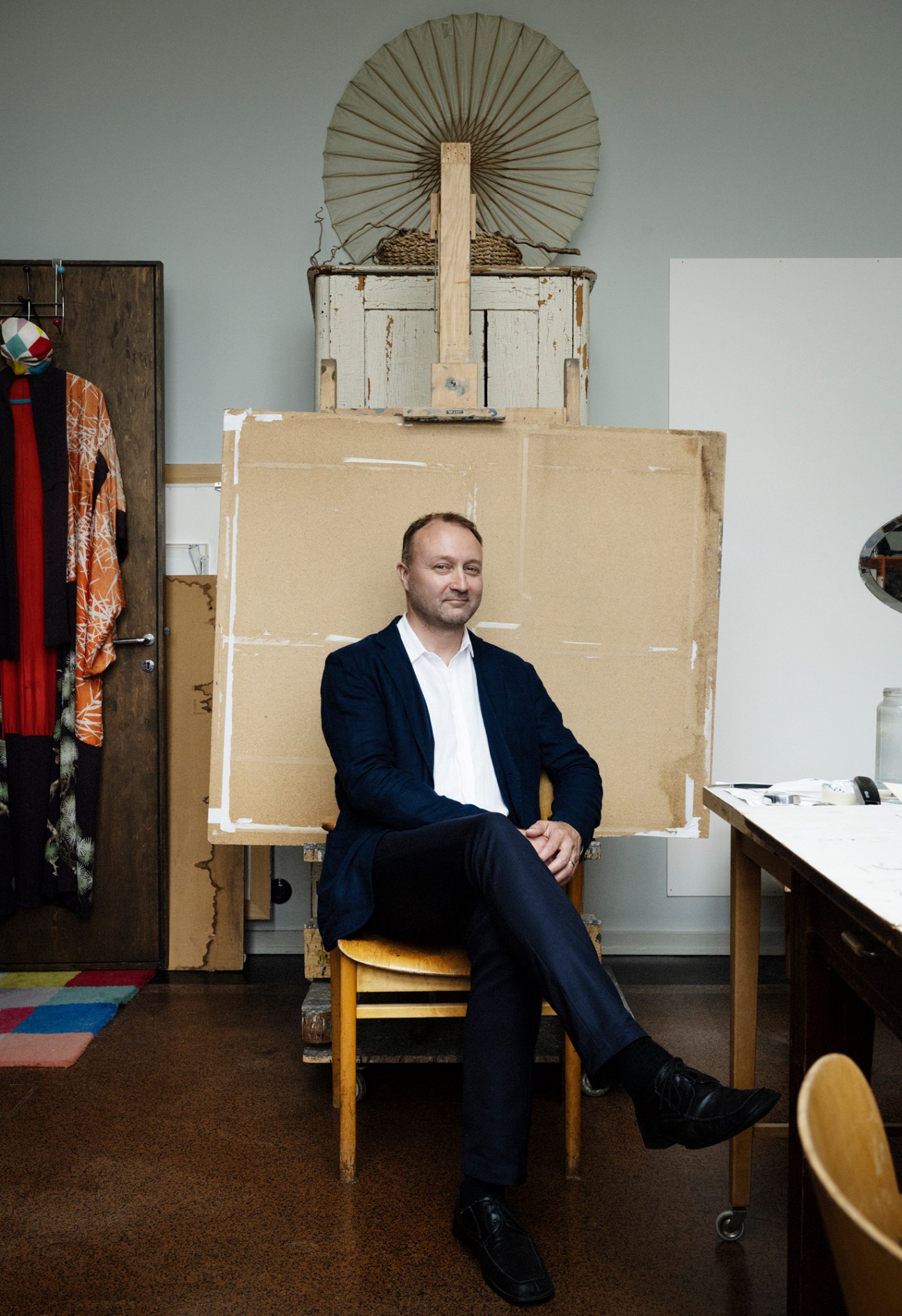 Mikko Mikkola sitting in an artist's studio surrounded by easels, art supplies, and creative materials