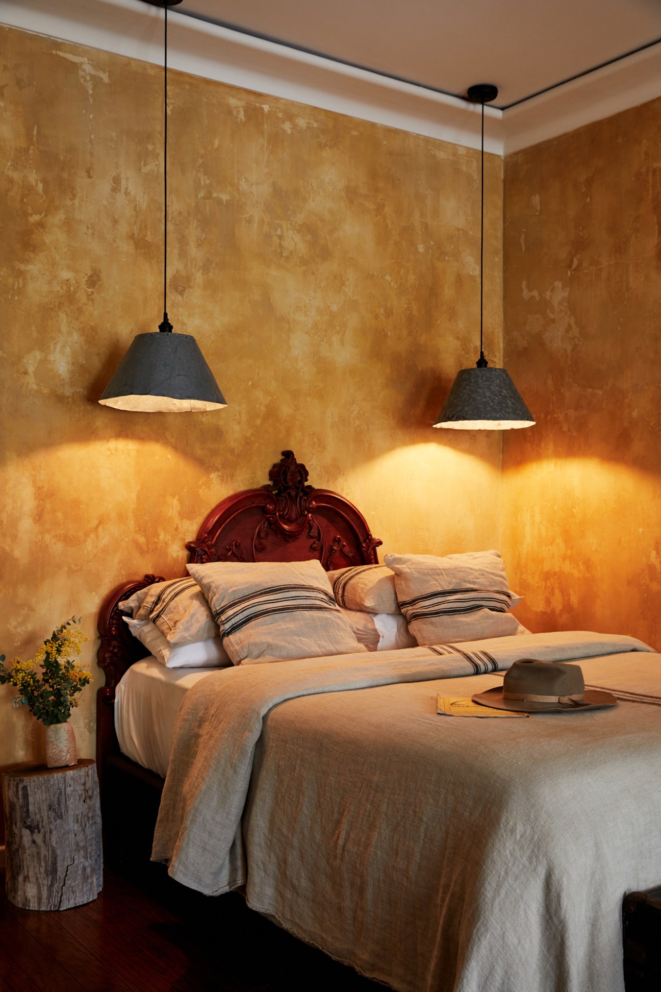 Warm bedroom interior with ornate headboard, pendant lights, and textured golden walls