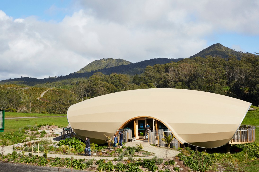Modern curved pod-shaped classroom building with natural timber entrance nestled in rolling green hills